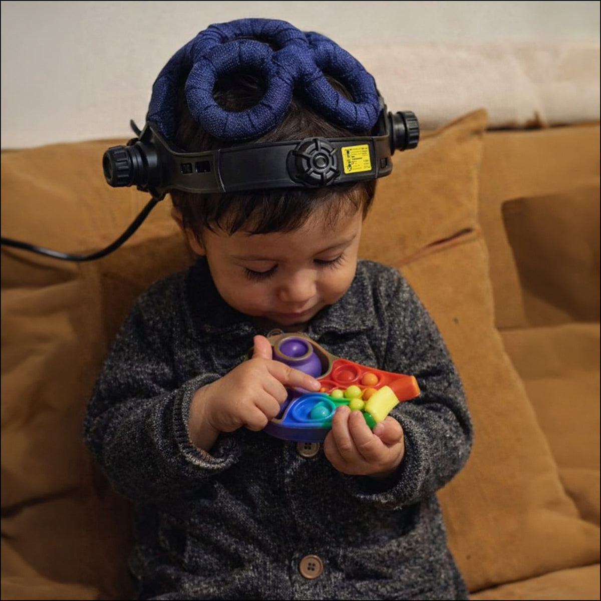 Young child sitting on a sofa wearing the QuantumMind TMS Helmet